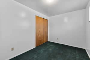 Empty room featuring baseboards and dark colored carpet