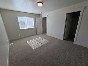 Unfurnished bedroom with a textured ceiling, carpet flooring, visible vents, and baseboards