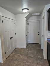 Corridor with a textured ceiling, stone finish floor, visible vents, and baseboards