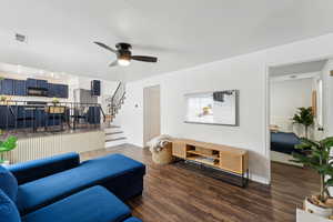 Living room with ceiling fan, stairs, visible vents, and dark wood finished floors