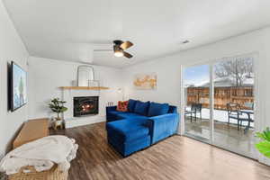 Living room featuring a ceiling fan, a brick fireplace, dark wood-style flooring, and visible vents