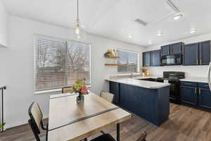 Kitchen with black appliances, blue cabinetry, pendant lighting, and light countertops