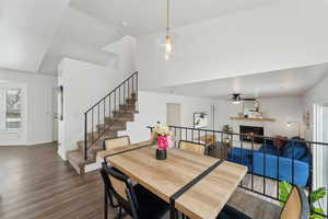 Dining room featuring dark wood-type flooring, ceiling fan, a lit fireplace, baseboards, and stairs
