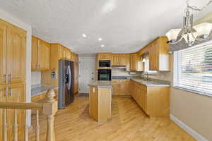 Kitchen with light wood-style flooring, a kitchen island, a sink, black appliances, and baseboards