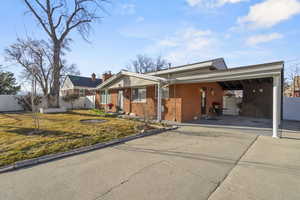 Single story home with brick siding, fence, driveway, a carport, and a front yard