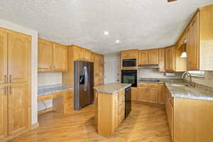 Kitchen featuring built in study area, a kitchen island, under cabinet range hood, black appliances, and a sink