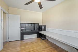 Home office with a wainscoted wall, ceiling fan, and wood finished floors