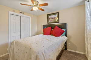 Carpeted bedroom with a textured ceiling, a ceiling fan, visible vents, baseboards, and a closet