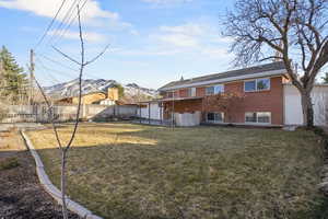 Back of property featuring a yard, brick siding, fence, and a mountain view