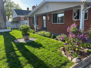 View of front facade with brick siding, a front lawn, a porch, and fence