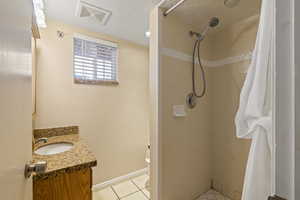 Full bathroom featuring baseboards, visible vents, tile patterned floors, a tile shower, and vanity