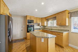 Kitchen featuring light wood finished floors, stainless steel fridge with ice dispenser, built in microwave, a sink, and black oven