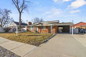 Ranch-style house featuring an attached carport, brick siding, fence, concrete driveway, and a front lawn