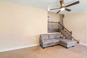 Living room featuring light carpet, baseboards, a ceiling fan, stairs, and a textured ceiling