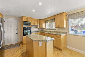 Kitchen featuring black appliances, a sink, a center island, and light wood-style floors