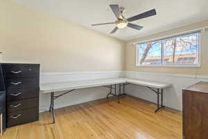 Office space featuring a textured ceiling, a wainscoted wall, wood finished floors, a ceiling fan, and built in study area