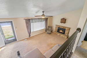 Living area featuring a textured ceiling, carpet floors, and a stone fireplace