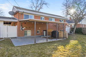 Back of property featuring a patio, brick siding, fence, a lawn, and a gate