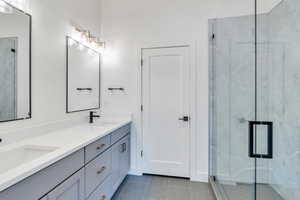 Full bathroom featuring a sink, a marble finish shower, and double vanity