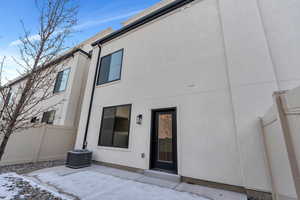 Snow covered house with central AC unit, a patio area, fence, and stucco siding