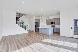 Kitchen with light countertops, appliances with stainless steel finishes, gray cabinets, a center island with sink, and pendant lighting