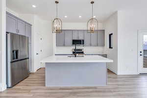 Kitchen with appliances with stainless steel finishes, a kitchen island with sink, pendant lighting, and light countertops