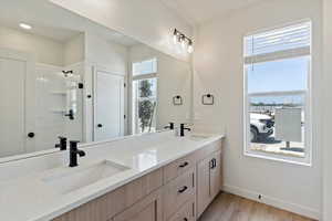 Bathroom featuring healthy amount of natural light, double vanity, tiled shower, and wood finished floors