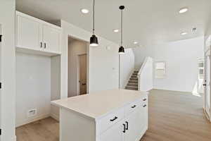 Kitchen featuring light wood-type flooring, a kitchen island, recessed lighting, white cabinets, and decorative light fixtures