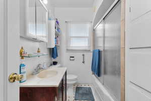 Bathroom with toilet, enclosed tub / shower combo, and vanity