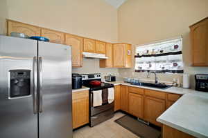 Kitchen with light tile patterned floors, under cabinet range hood, a sink, light countertops, and appliances with stainless steel finishes