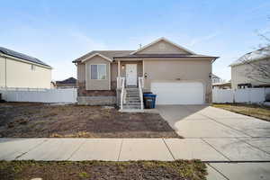 View of front facade with driveway, stone siding, a garage, and fence