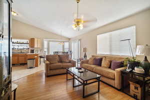 Living room featuring light wood-style floors, vaulted ceiling, a textured ceiling, and ceiling fan with notable chandelier