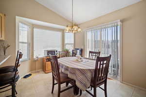 Dining room with vaulted ceiling, light tile patterned floors, baseboards, and a notable chandelier