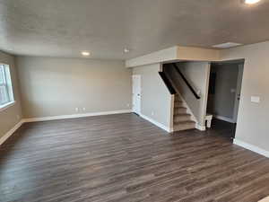 Empty room featuring dark wood-type flooring, a textured ceiling, baseboards, and stairs