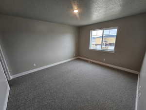 Empty room with a textured ceiling, carpet flooring, visible vents, and baseboards