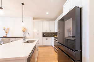 Kitchen featuring a sink, light countertops, appliances with stainless steel finishes, decorative backsplash, and light wood finished floors