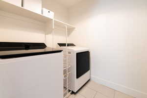 Washroom with washing machine and dryer, laundry area, baseboards, and light tile patterned floors