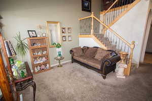 Carpeted living room featuring a high ceiling, stairs, and baseboards