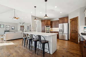 Kitchen featuring a breakfast bar area, appliances with stainless steel finishes, wood-type flooring, decorative light fixtures, and a large island with sink