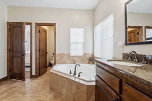 Bathroom featuring vanity, a relaxing tiled tub, tile patterned floors, and toilet