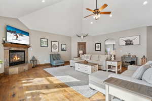 Living room featuring a fireplace, vaulted ceiling, ceiling fan, and light wood-type flooring