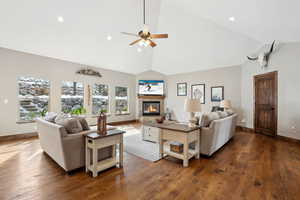 Living room with a tiled fireplace, high vaulted ceiling, dark hardwood / wood-style floors, and ceiling fan