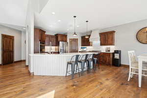 Kitchen featuring custom exhaust hood, pendant lighting, stainless steel appliances, a large island, and hardwood / wood-style floors