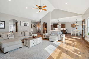 Living room with high vaulted ceiling, ceiling fan with notable chandelier, and light hardwood / wood-style floors