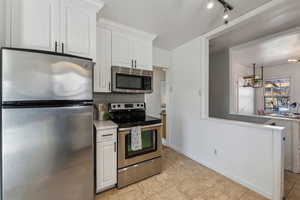 Kitchen featuring tasteful backsplash, white cabinets, appliances with stainless steel finishes, light countertops, and light tile patterned flooring