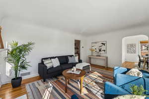 Living room with visible vents, arched walkways, light wood-style flooring, and baseboards