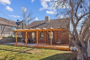 Rear view of property featuring brick siding, a lawn, a shingled roof, and fence