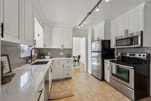 Kitchen featuring decorative backsplash, appliances with stainless steel finishes, white cabinets, and a sink