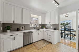 Kitchen featuring decorative backsplash, white cabinets, dishwasher, light countertops, and a sink