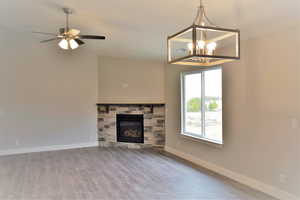 Unfurnished living room with lofted ceiling, ceiling fan with notable chandelier, wood finished floors, a fireplace, and baseboards